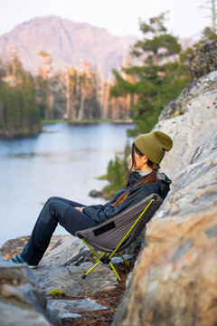 Woman sitting in camping chair looking at view of lake in wilderness