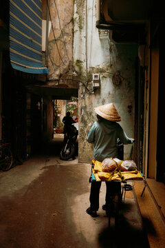 Street vendor pushes cart in narrow alley during day in Vietnam