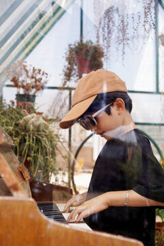 Chinese boy plays the piano in a glasshouse in a garden.