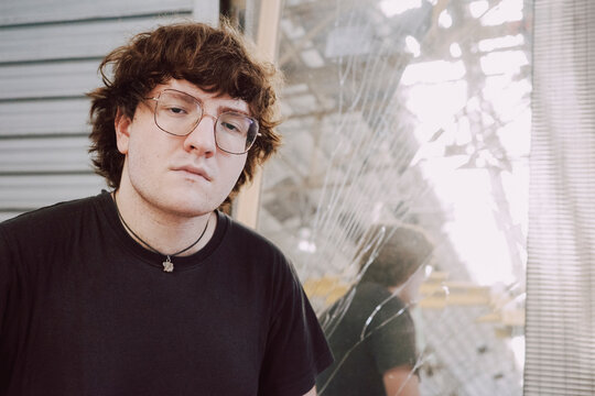 Young Man Poses in Front of Broken Window 
