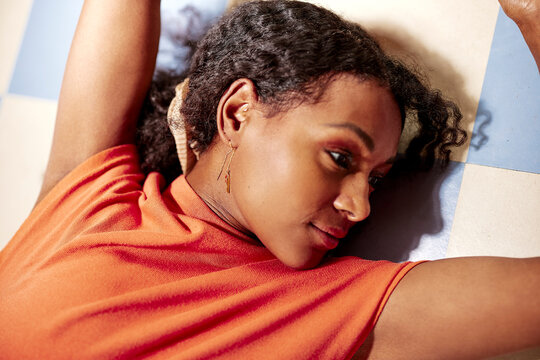 Relaxed Beautiful Black woman resting on a tiled cafe floor in an orange shirt with a calm, peaceful expression