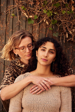 Two diverse women embrace in cozy knitwear, showcasing friendship and warmth in autumn tones