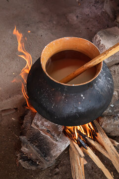 Clay pot simmering over wood fire with steam