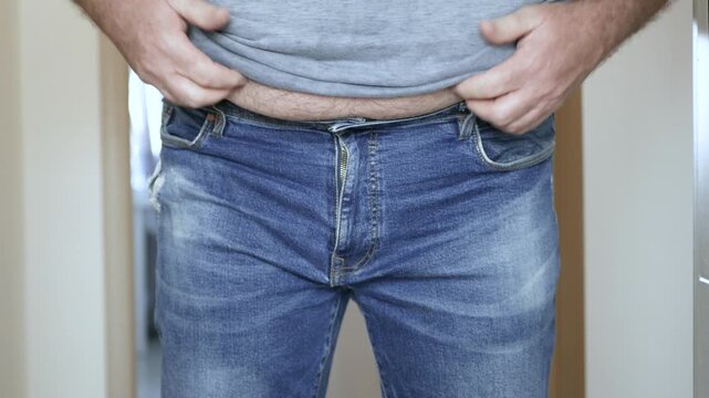 Overweight Man Struggling to Fasten Belt on Jeans Closeup. Man with Big Belly Trying to Buckle Leather Belt.