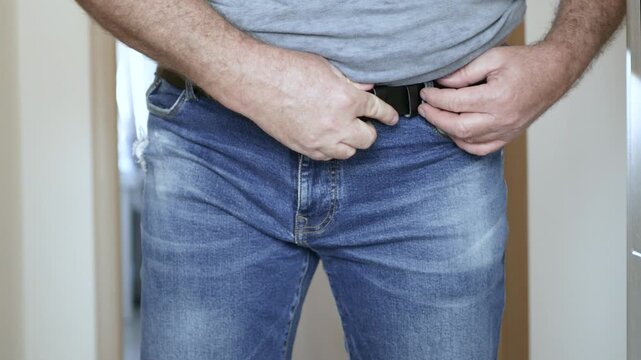 Overweight Man Struggling to Fasten Belt on Jeans Closeup. Man with Big Belly Trying to Buckle Leather Belt.