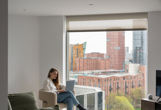 Woman Using Computer in Apartment With City View