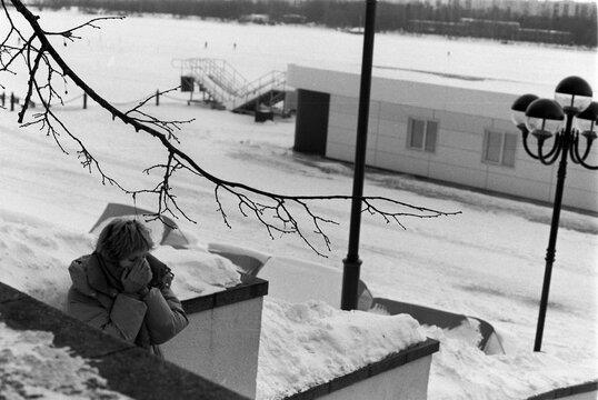 Solitary figure resting by winter waterfront on 35mm film