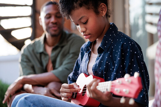Girl practices ukulele, father watches.