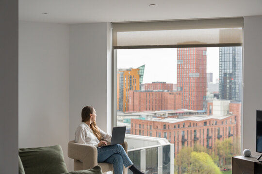 Woman With Computer Near a Large Window To The City