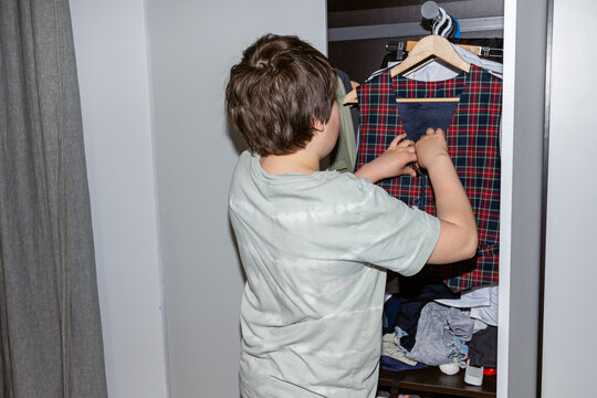 A boy hangs clothes in the closet