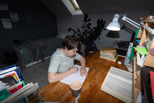 A schoolboy reading a book at a wooden table