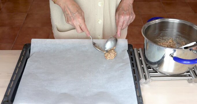 Female hands shaping meringue and nut cookie mixture into small mounds on baking tray lined with parchment paper.