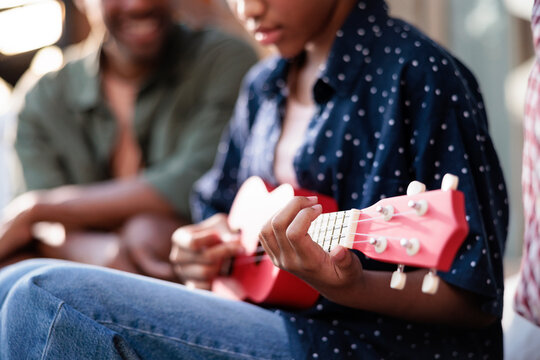 Girl playing ukulele while father sits nearby outdoors