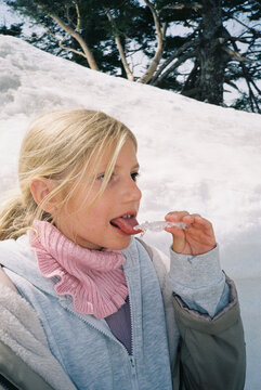 A girl is licking a piece of ice outdoors in winter