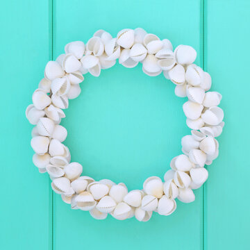 Cockleshell white seashell natural wreath on rustic turquoise wood background. Round shape garland decoration symbol of summer seaside.