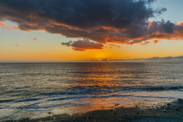 Obraz premium View of the sunset from the seashore. A beautiful sunset that colors the horizon and clouds in orange colors