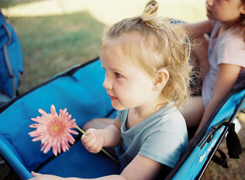 Young Girl Holding Flower While Sitting in Beach Wagon.