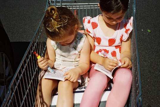Sisters drawing in books while waiting beside car in trolley.