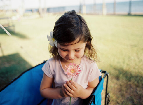 Young Girl Holding Pink Flower with flower in her hair  in beach wagon