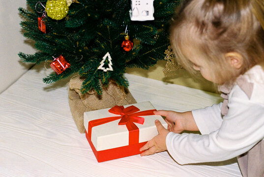 Little girl in dress puting gift box under the Christmas tree.