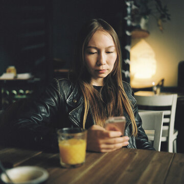 Young Woman Using Smartphone at a Caf&eacute; Table in Warm Light