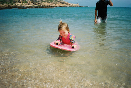 Father Helping Young Girl on Bodyboard at Beach in Bowen