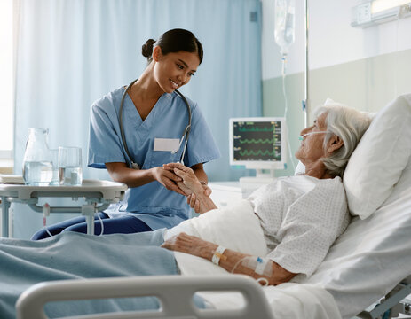 Nurse assisting elderly patient in hospital bed with medical equipment and IV drip