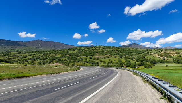 Empty asphalt road winding through green hills under a bright blue sky, Koyulhisar, Sivas, Turkey.