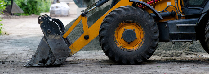 Yellow backhoe loader parked on a dirt path with construction materials nearby. Concept of urban infrastructure improvement, landscape design, and sidewalk reconstruction. Photo © slexp880
