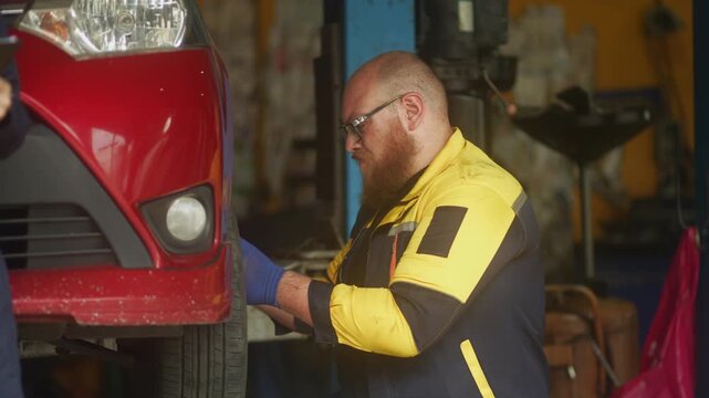 Caucasian male mechanic with glasses and a beard works alongside a female technician, reviewing a digital tablet and giving a thumbs-up. This high-energy commercial imagery represents gender diversity