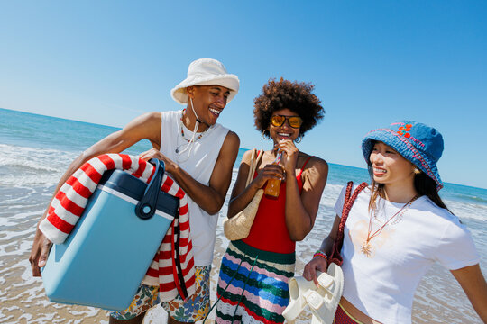 Friends enjoying summer beach holiday carrying cooler