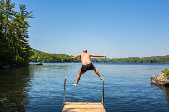 Middle age man jumping off a dock on vacation on a lake in Maine. 
