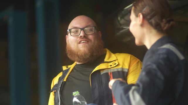 Caucasian male mechanic with glasses and a beard works alongside a female technician, reviewing a digital tablet and giving a thumbs-up. This high-energy commercial imagery represents gender diversity