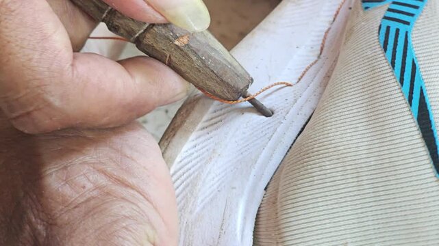 Close up view of a cobbler hand stitching the sole of a sports shoe using an awl and heavy thread
