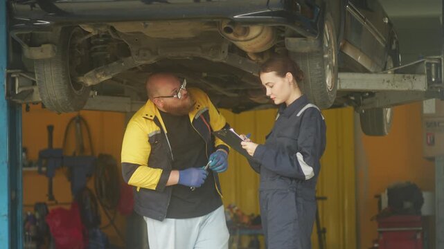 Caucasian male mechanic with glasses and a beard works alongside a female technician, reviewing a digital tablet and giving a thumbs-up. This high-energy commercial imagery represents gender diversity