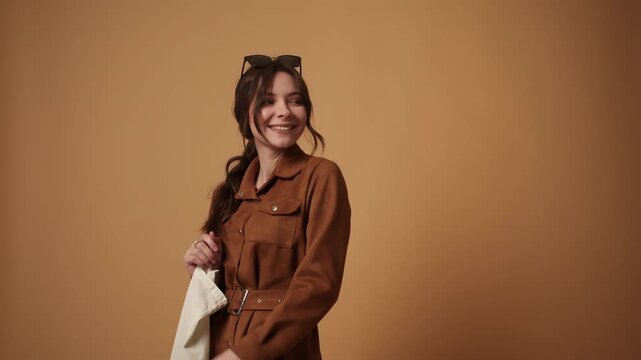 Stylish young woman dancing happily and posing with an eco-friendly tote bag against a brown background