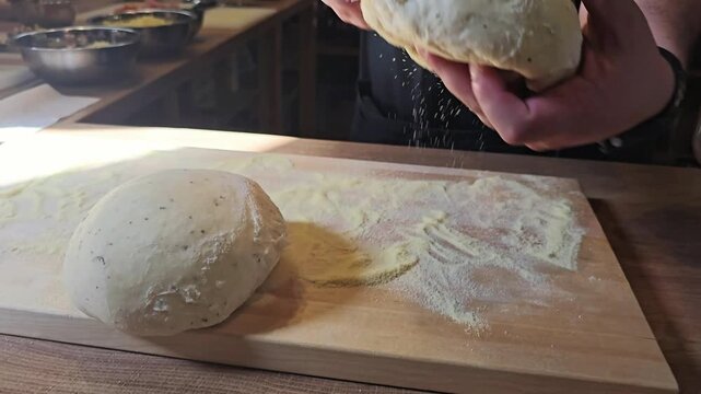 A man's hands take one of the two pieces of raw dough to make pizza