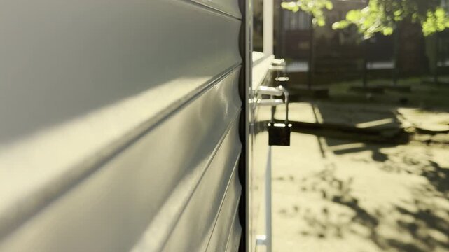 A closed metal roller shutter locks a kiosk in a sunny park.