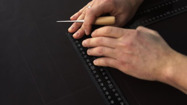 Leatherworker marking black leather with a scribe and ruler creating a custom handmade pattern for crafting products