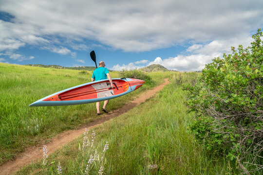 senior male paddler is carrying a long racing stand up paddleboard (SUP) uphill on a trail in early summer - Lory State Park, Colorado