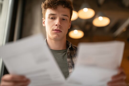 Young man reading and comparing insurance documents indoors