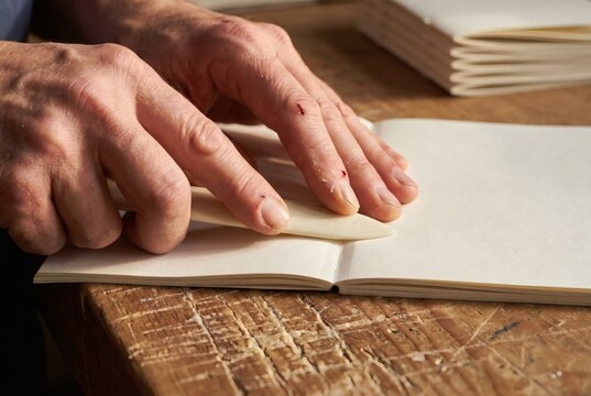 Master Bookbinder Hands Pressing Fold with Bone Folder on Paper Signatures Traditional Bookbinding Craftsmanship Concept