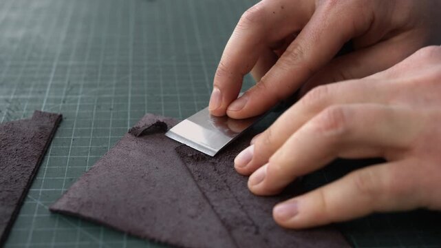 Artisan hands skiving dark leather with a sharp blade on a cutting mat for a custom handcrafted accessory
