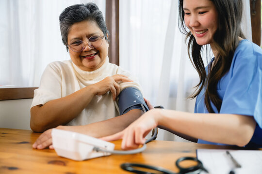 Young nurse checks senior is blood pressure with digital sphygmomanometer. Senior woman smiles warmly at healthcare interaction. Nurse shows calm, professional demeanor during exam