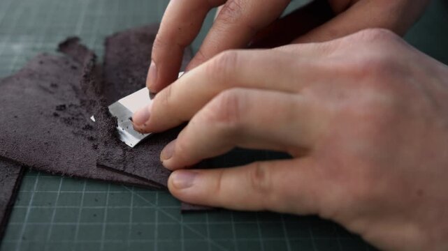 Leatherworker skiving and thinning genuine leather with a sharp blade on a cutting mat in a traditional workshop