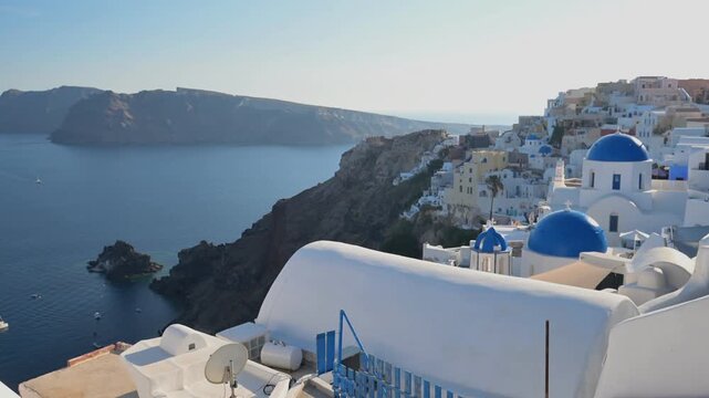 Scenic summer view of Oia&rsquo;s whitewashed architecture and blue domes overlooking the Aegean Sea and volcanic cliffs in Santorini, Greece.