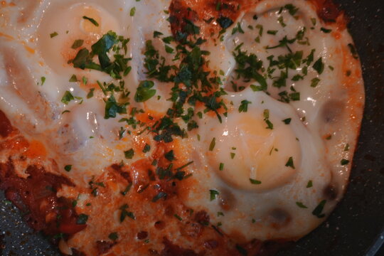 Appetizing Fried Eggs in Pan with Parsley and Red Sauce Breakfast Overhead Close Up Healthy Food Cuisine, shakshouka