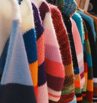 Vibrant Row of Colorful hand-knitted Striped Sweaters Hanging on a Clothing Rack Artisanal Fashion Textile Collection Cozy Winter Warm Apparel