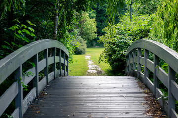 Obraz premium Wooden footbridge surrounded by willow branches in romantic garden park scenery