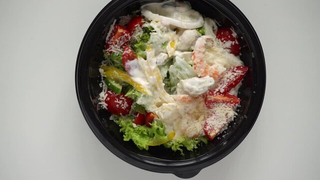 Woman eating a fresh seafood caesar salad with a fork from a bowl isolated on a white background, top view